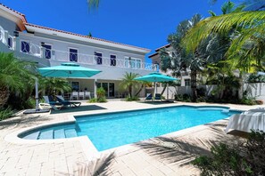 Ein Swimmingpool mit Liegestühlen und Sonnenschirmen, umgeben von Palmen und einem Gebäude mit einem Balkon.