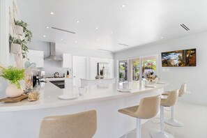 A modern kitchen with white cabinetry, a central island with bar stools, and a large window offering a view of the outdoors.