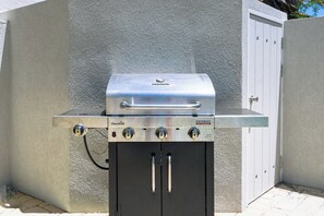 A Char-Broil gas grill with a metal cabinet below it, set against a textured wall with a white door in the background.