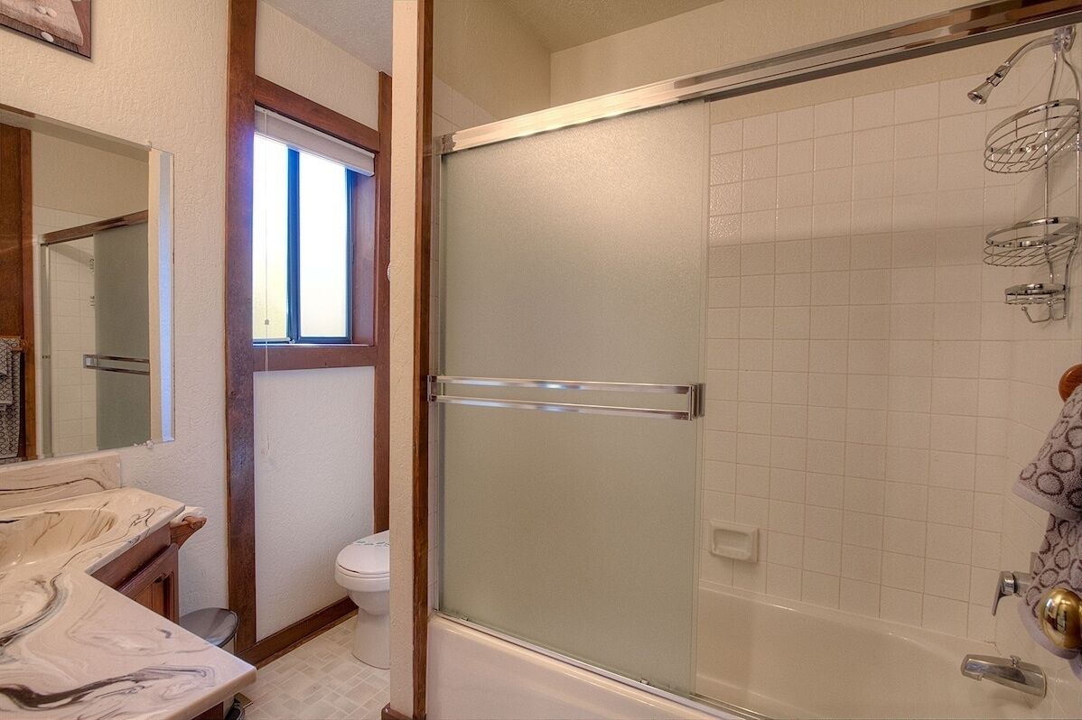 A bathroom with a glass-enclosed shower, a toilet, and a marble sink.