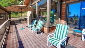 A covered outdoor seating area with striped chairs and a table, large windows, and a wooden deck.
