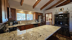 Una cocina con encimeras de granito, armarios de madera, refrigerador de acero inoxidable y horno empotrado.