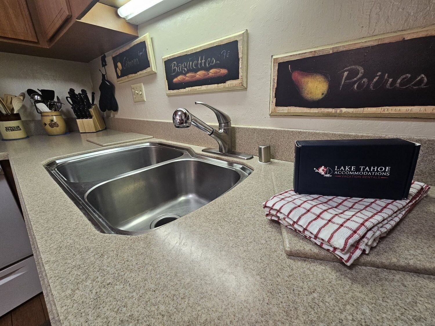 A kitchen with a double stainless steel sink, a coffee maker, and a sign for Lake Tahoe Accommodations.