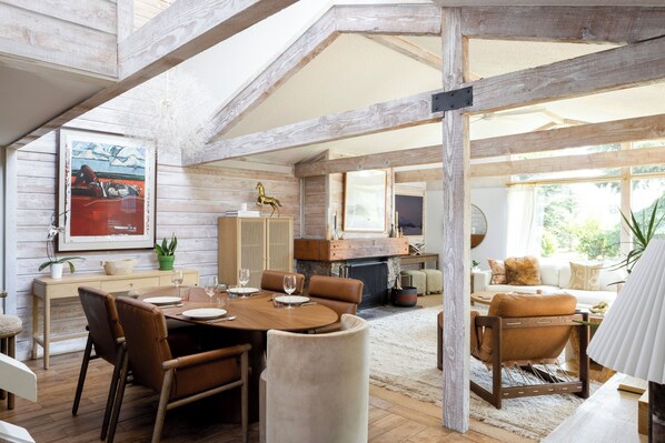 A spacious room with a wooden ceiling, a dining area with a round table and chairs, a fireplace, and a sofa with cushions.