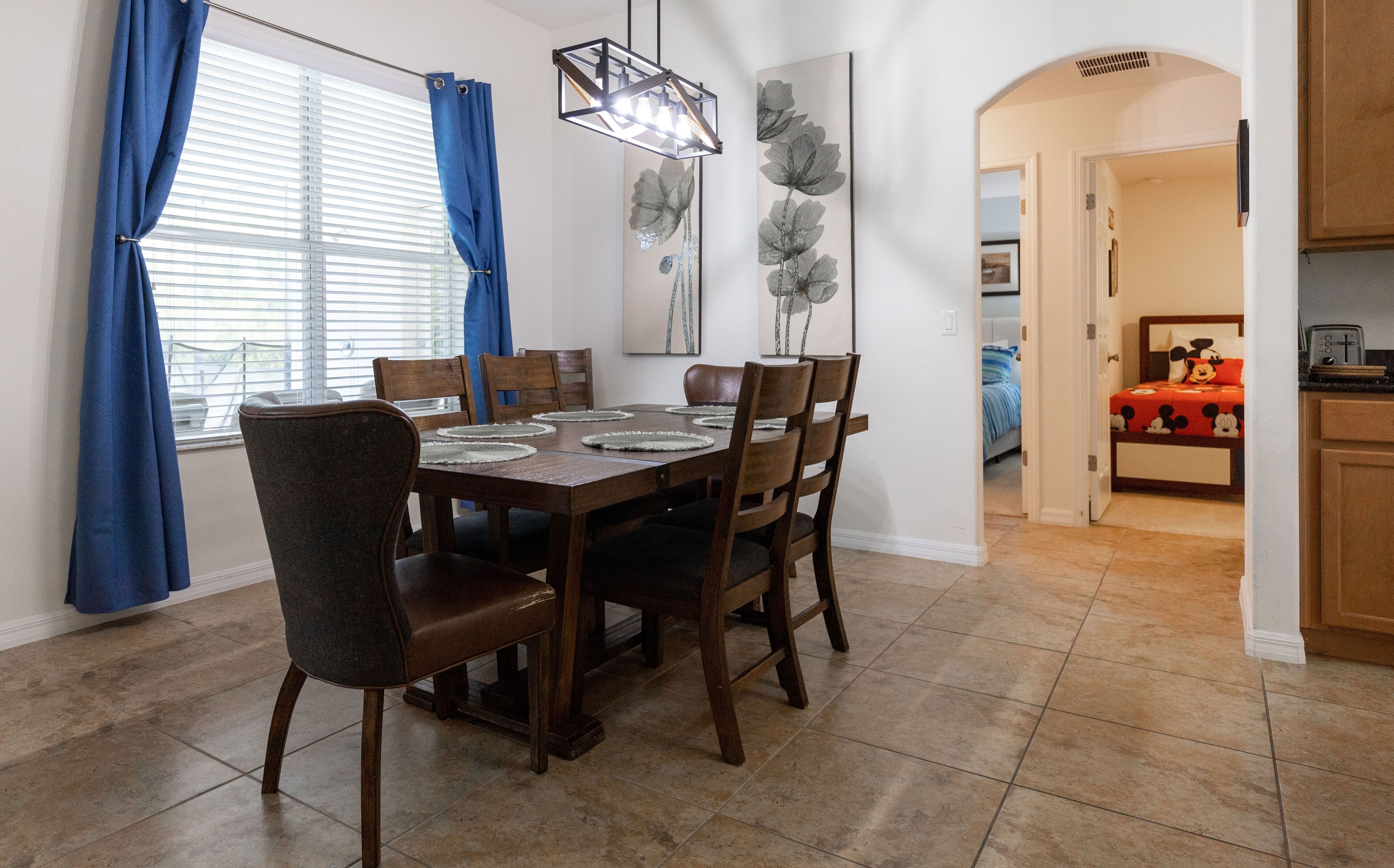 A dining area with a wooden table and chairs, blue curtains, and a modern light fixture.