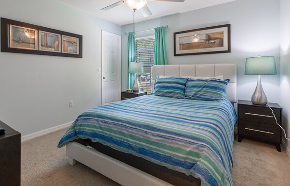 Une chambre à coucher avec un lit, des tables de chevet, un ventilateur de plafond et des œuvres d’art accrochées aux murs.