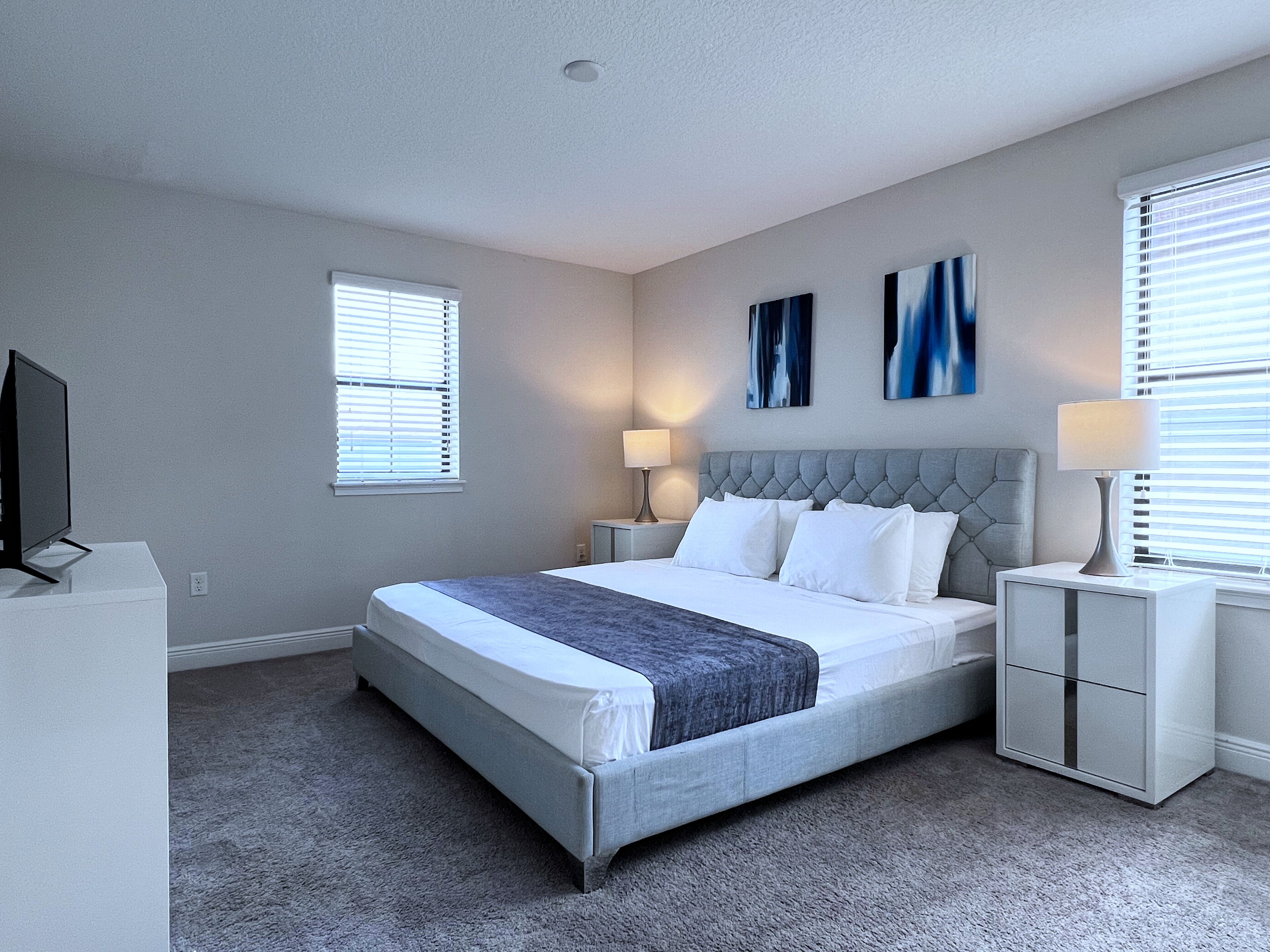 A bedroom with a large bed, two bedside tables, a TV, and artwork on the wall.