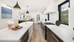 A modern kitchen with white countertops, black pendant lights, and a large window.