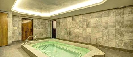 Una amplia piscina interior con suelo y paredes de azulejos, rodeada por un techo alto con tragaluces.