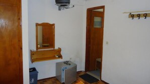 A small, compact room with a wooden door, a mirror, a television mounted on the wall, a small refrigerator, and a heater.