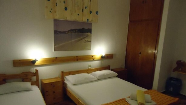 A room with two single beds, wooden headboards, a nightstand with a lamp, a wooden wardrobe, and a framed picture on the wall.