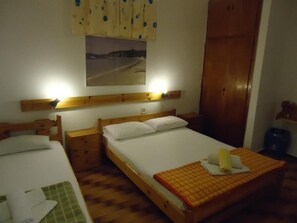 Een kamer met twee eenpersoonsbedden, houten hoofdborden, een nachtkastje met lamp, een houten garderobe en een gekaderd schilderij aan de muur.