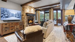 A cozy living room with a stone fireplace, leather furniture, and a large TV on the wall. - 1138 Skiers Heaven! Luxury Home Close To Park City Mountain! Two Hot Tubs & Gorgeous Outdoor Space! 6 Bedroom Home by RedAwning (Park City)