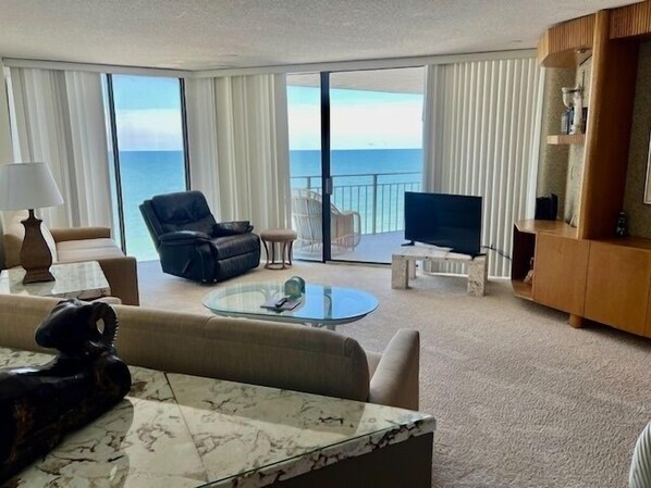 A hotel room with a large balcony, a sofa, a coffee table, a TV, and a wooden cabinet.
