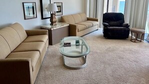 Ein modernes Wohnzimmer mit einem beige gefärbten Sofa, einem schwarzen Ledersessel, einem Glastisch und einem kleinen Beistelltisch mit Lampe.