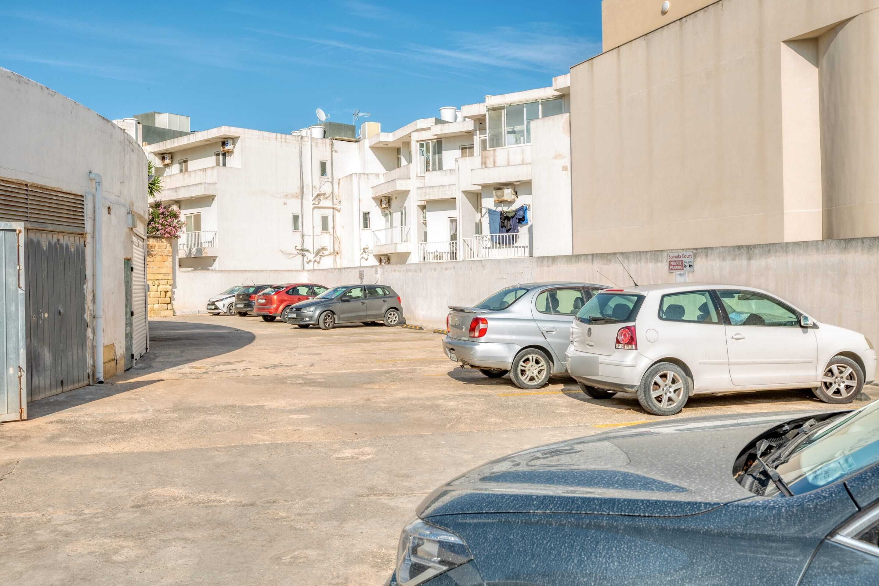 Un'area di parcheggio con diverse auto, un edificio con balconi e un cartello che indica il costo del parcheggio.