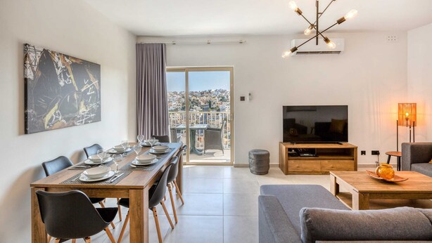 A modern living room with a dining area, a TV, and a large window with a city view.