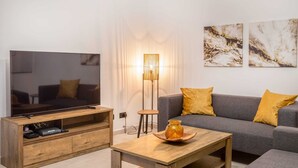 A modern living room with a flat-screen TV, wooden coffee table, grey sofa, and yellow cushions.