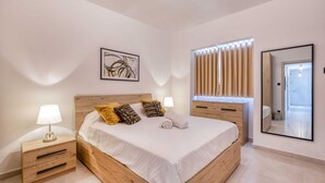 A bedroom with a wooden bed, two bedside tables, a nightstand, a wall-mounted mirror, and a window with curtains.