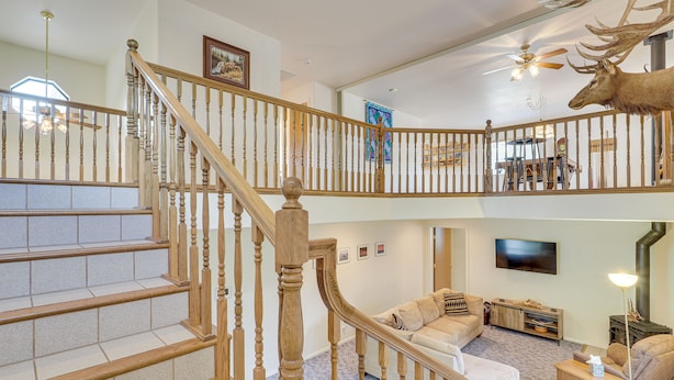 A two-story home with a wooden staircase, a living room with a sofa and a television, and a deer head decoration on the upper floor. - Charming Elko Home w/ Pool Table! (Elko)