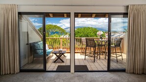 A balcony with a sliding glass door, a seating area with a sofa and a table, and a view of a green landscape and mountains.