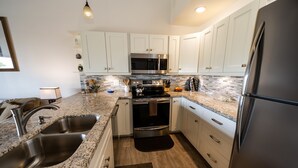A modern kitchen with white cabinets, stainless steel appliances, granite countertops, and a wooden floor.