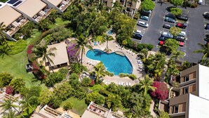 An aerial view of a resort with a central swimming pool surrounded by palm trees and lounge chairs.