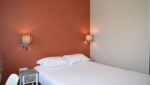 A hotel room with a single bed, two wall-mounted lamps, a small bedside table with a lamp, and a chair. - Résidence Voltaire (Châteauroux)