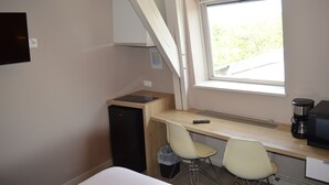 A compact room with a kitchenette, a small fridge, a desk with a chair, a window, and a TV mounted on the wall. - Résidence Voltaire (Châteauroux)