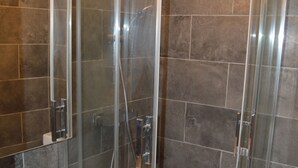 A modern bathroom with a glass-enclosed shower, a white sink, and dark tiled walls. - Résidence Voltaire (Châteauroux)