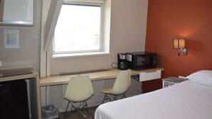 A hotel room with a bed, a desk with a computer, a chair, a microwave, and a window with a view of trees. - Résidence Voltaire (Châteauroux)