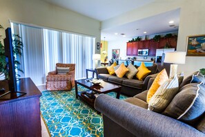 Relax in this stylish living room with a sofa set, coffee table, and TV on a stand, surrounded by a patterned rug and large window with blinds.