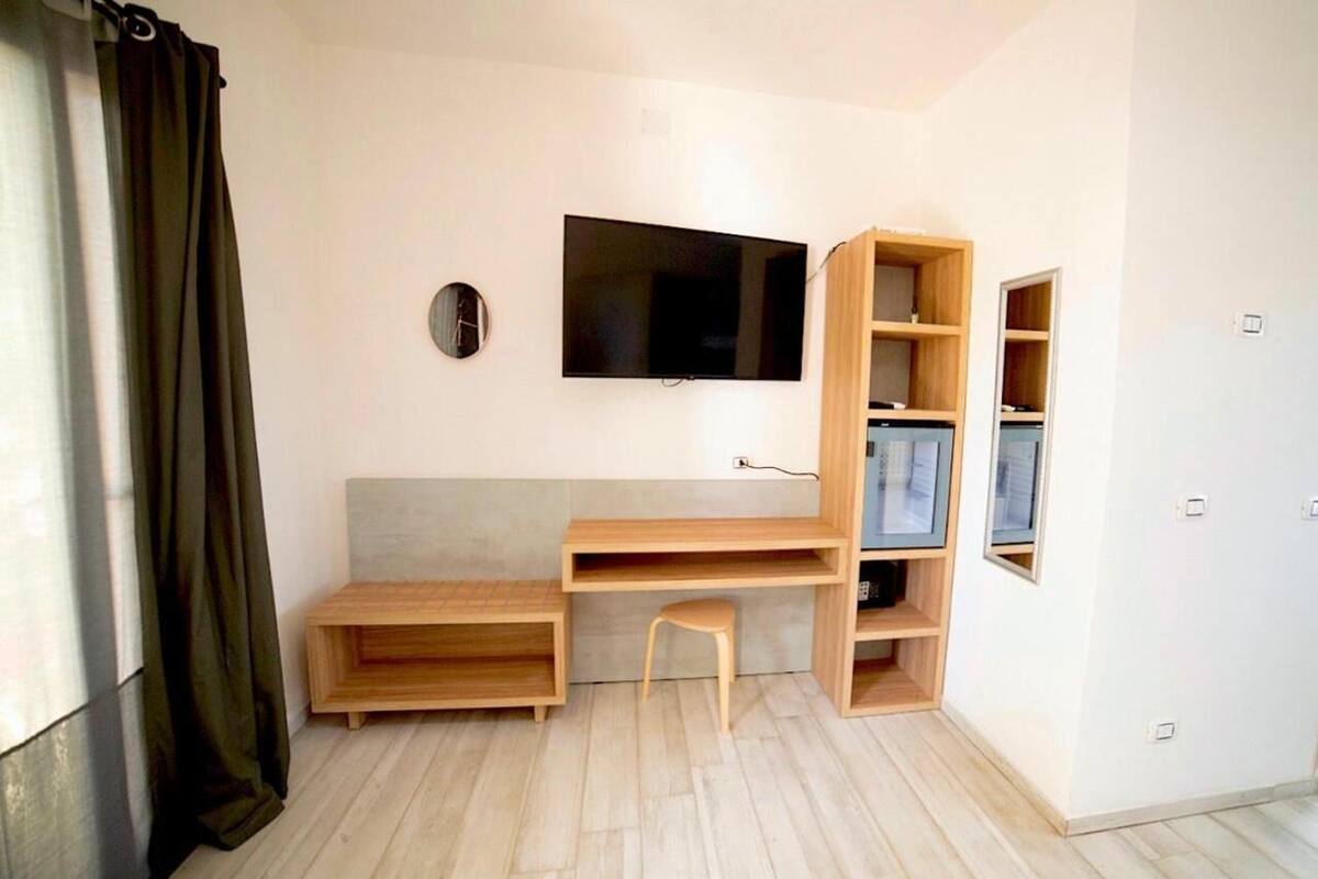 A room with a wooden desk, a chair, a television mounted on the wall, and built-in shelving.