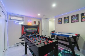 A room with a foosball table, neon signs, and LED strip lights.