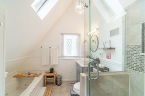 A modern bathroom with a skylight, a glass-enclosed shower, a wooden bench, and a small trash bin.