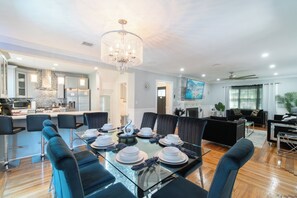 A modern kitchen with a stone backsplash, a dining area with a glass table and black chairs, and a living area with a black sofa and a fireplace.