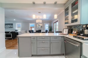 A modern kitchen with a central island, pendant lights, and a view into the dining area.