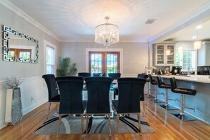 A modern kitchen with a bar area, a chandelier, and a dining area with chairs.
