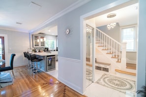 A modern kitchen with bar stools, a dining area with a table and chairs, and a staircase leading to an upper floor.