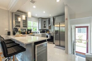 Une cuisine moderne dotée d’un îlot central, d’appareils électroménagers en acier inoxydable et de luminaires suspendus.