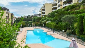 A swimming pool with lounge chairs and umbrellas, surrounded by greenery and residential buildings. - Happyfew La terrasse de Flora (Nice)