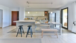 A modern kitchen with a central island, bar stools, a dining table, and a bench. - Happyfew La terrasse de Flora (Nice)
