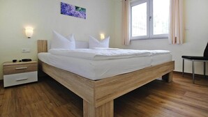 Ein modernes Schlafzimmer mit einem Bettgestell aus Holz, einem Nachttisch mit Schubladen, einem Sessel und einem Fenster mit Vorhängen.