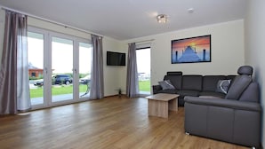 Ein modernes Wohnzimmer mit einem grauen Sofa, einem Holztisch und einem flachbildfernseher an der Wand.