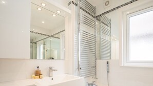 Ein modernes Badezimmer mit einem weißen Waschtisch, einem großen Spiegel, einer Duschkabine aus Glas und einem Fenster.