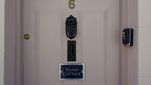 Uma porta com o número 6, uma maçaneta de latão, um interfone e uma placa que diz 'Blush Cottage'.