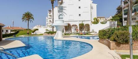 Relax by the resort pool surrounded by a low concrete deck and palm trees.