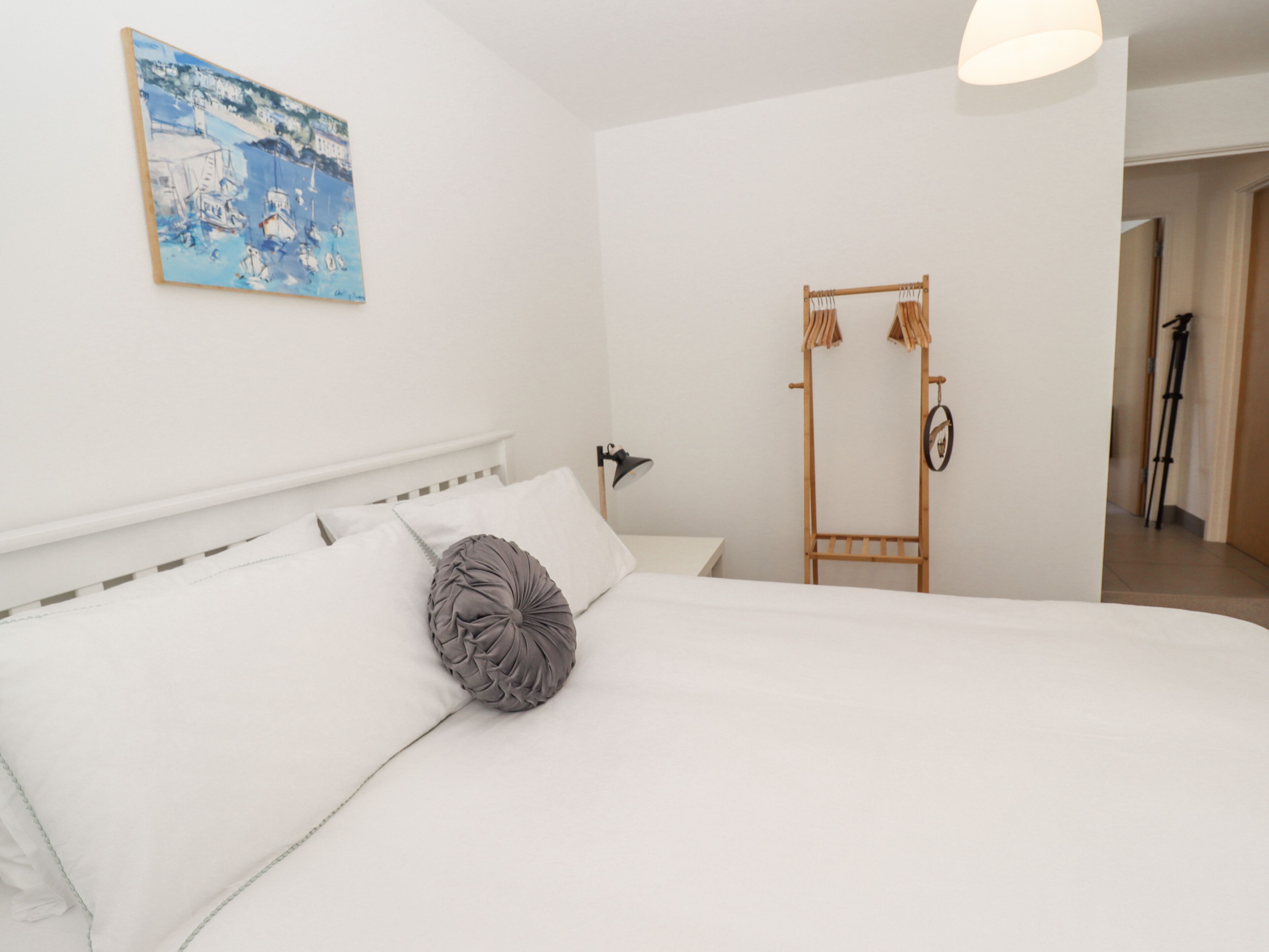 A bedroom with a bed, a painting, a wooden drying rack, and a lamp.