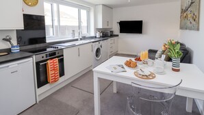 Ett modernt kök med tvättmaskin, ett matbord med frukostmat och en TV som är monterad på väggen.