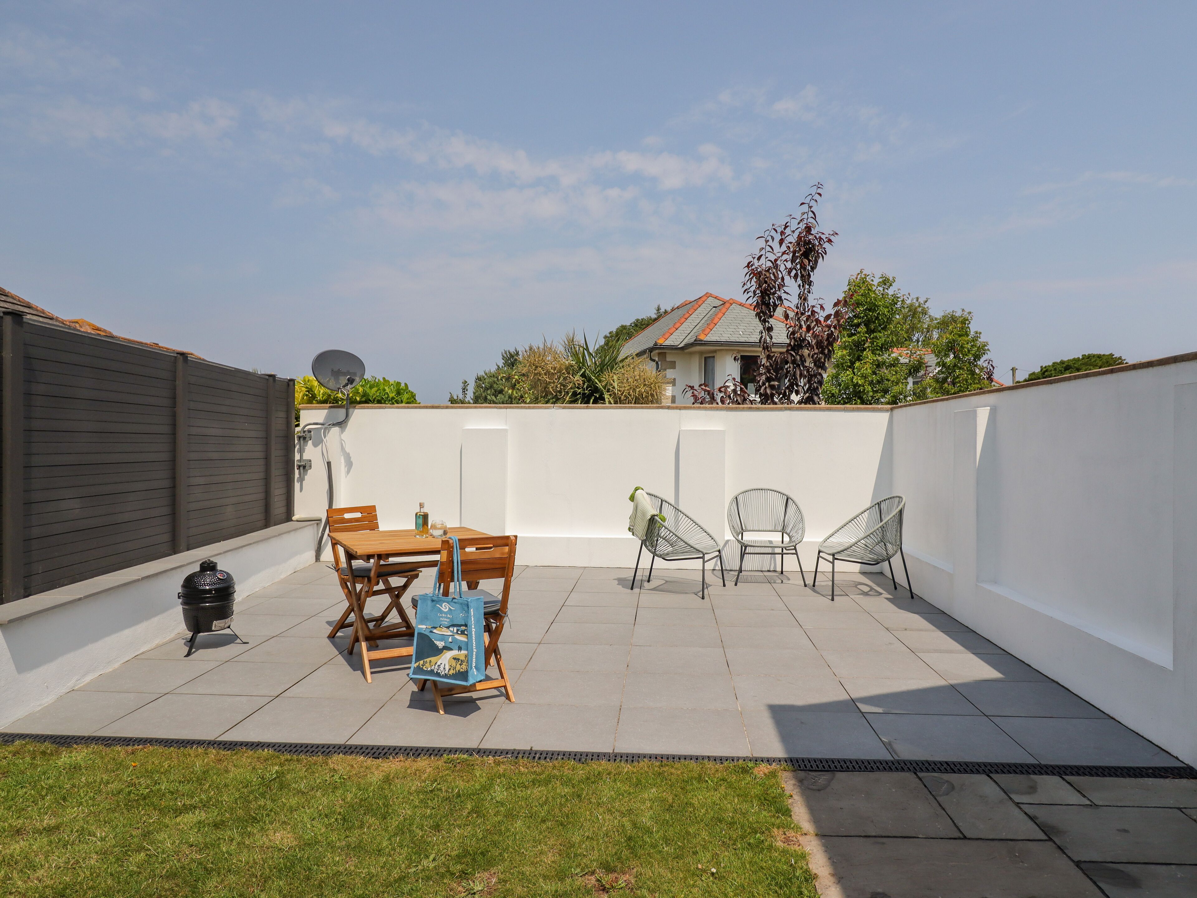 A rooftop patio with a wooden table and chairs, a barbecue grill, and a satellite dish.